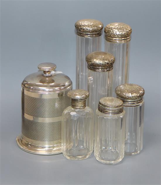 A George V engine turned silver cigarette dispenser, Birmingham, 1935 and six silver lidded glass toilet jars.